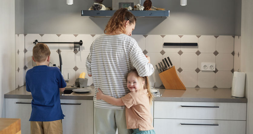 flicka med down syndrom kramar sin mammas ben i köket