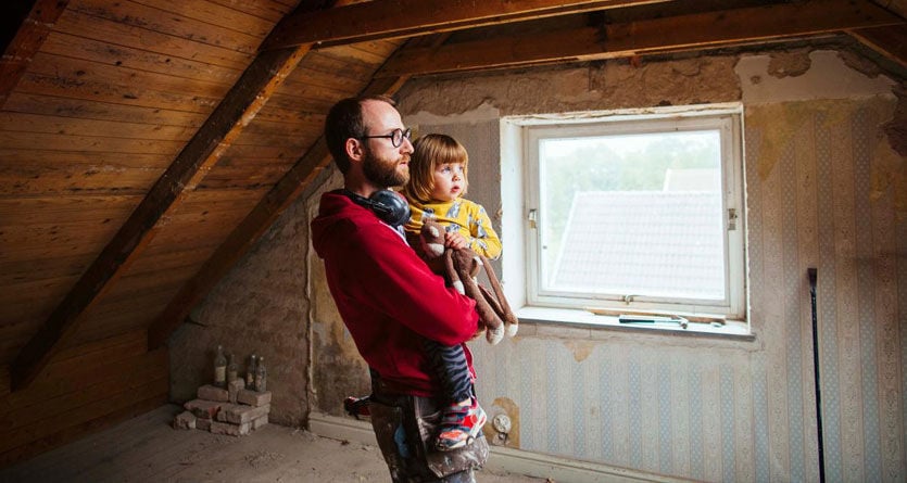 Pappa inspekterar vinden i huset med sitt barn i famnen