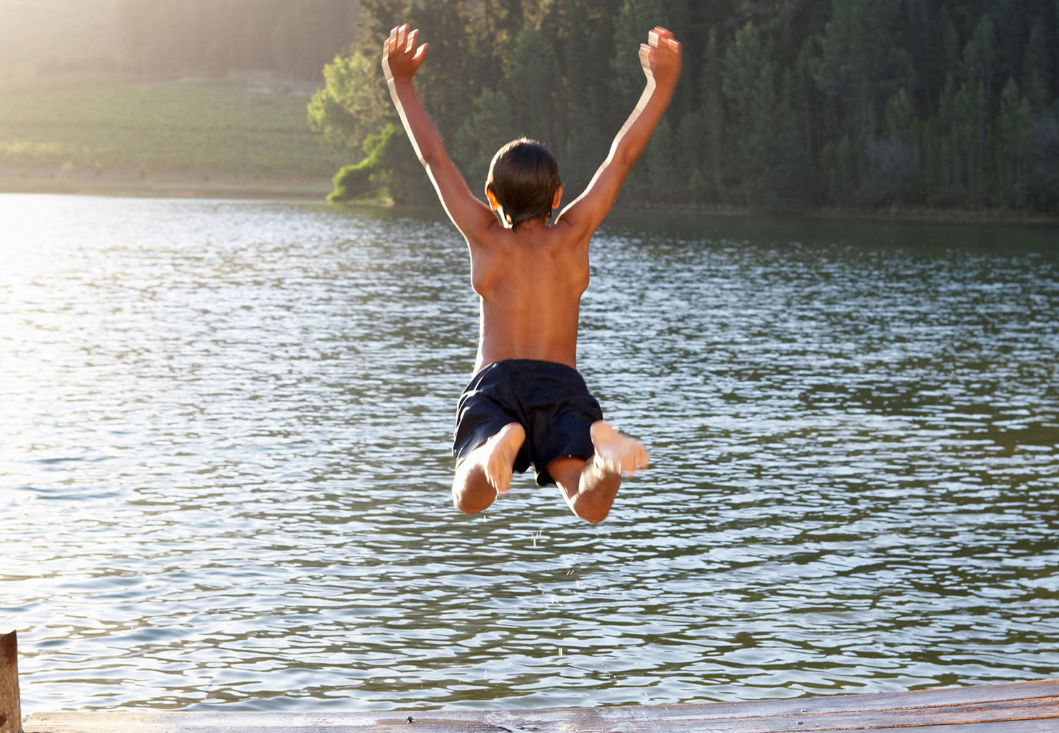 Pojke hoppar i vattnet från brygga