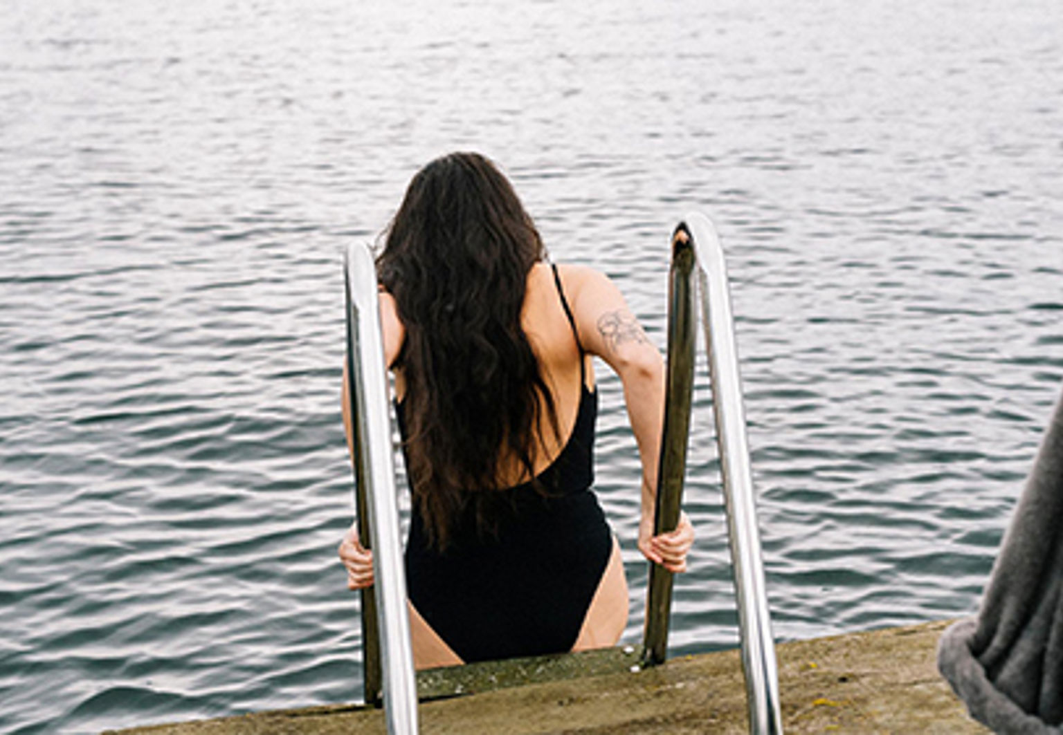 Kvinna med långt hår kliver ner i vatten på en stege