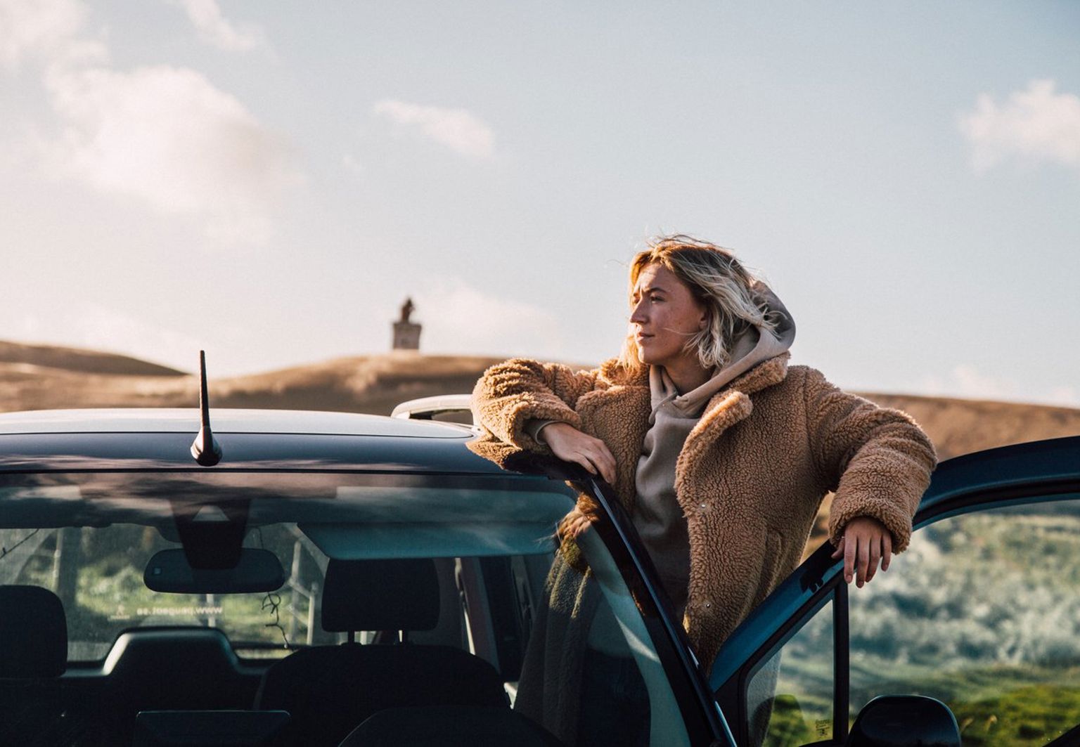 Kvinna står vid en öppen bildörr på ett stort fält