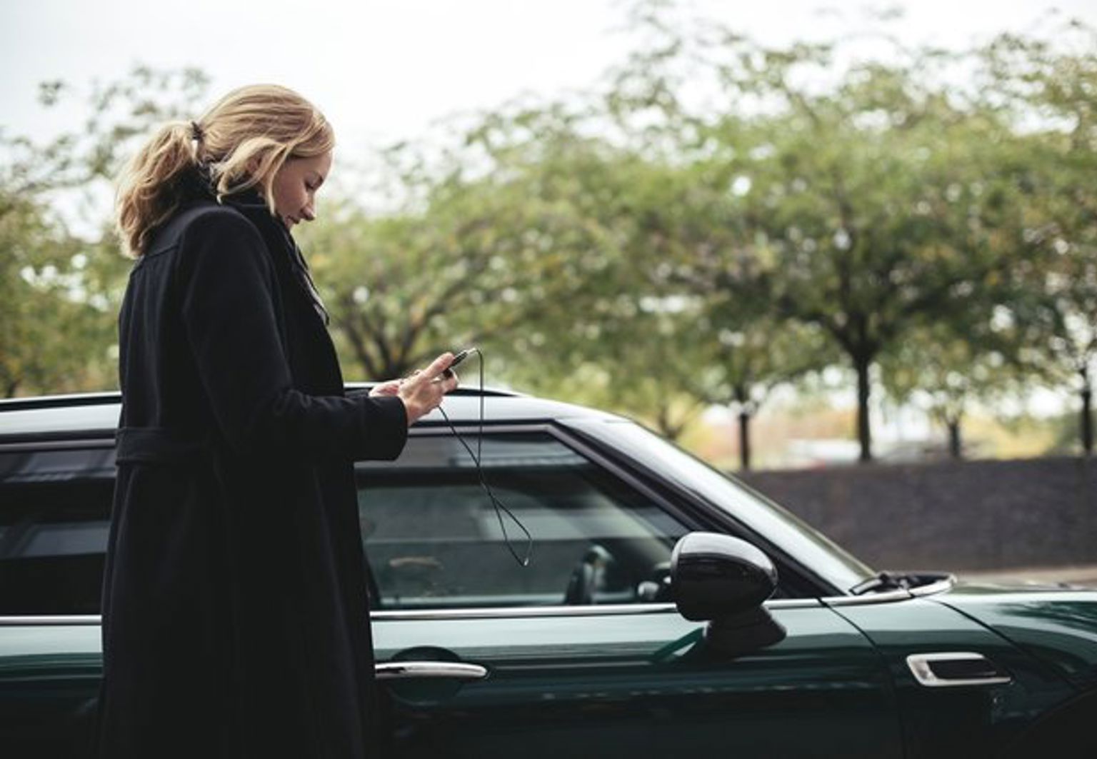 Kvinna tittar på sin telefon bredvid sin parkerade bil