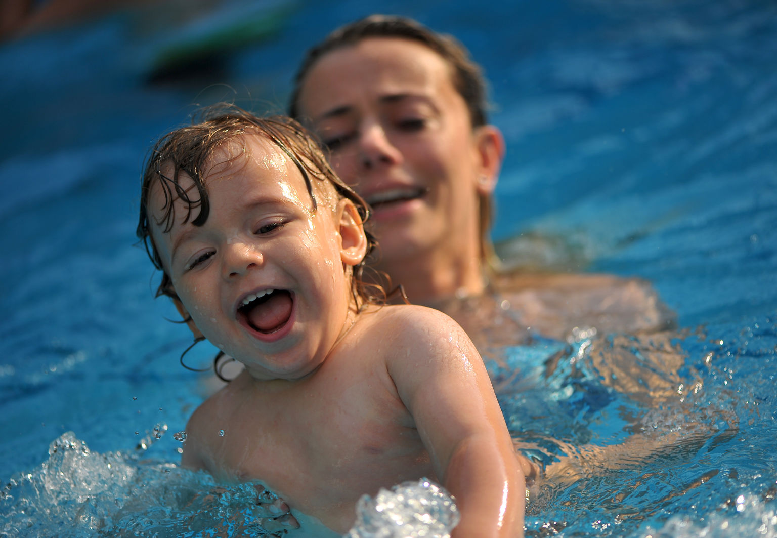 Mamma simmar med sitt glada barn i en pool