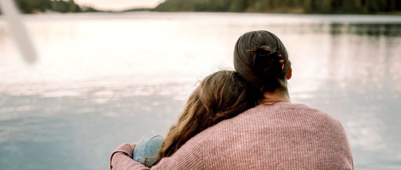 mamma håller om sin dotter vid en sjö
