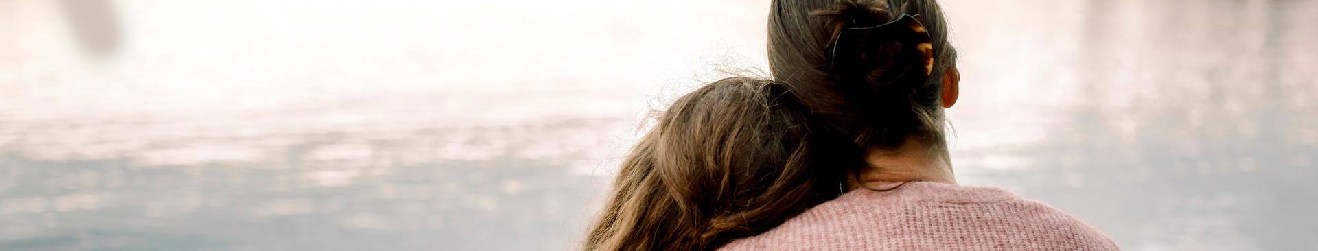 mamma håller om sin dotter vid en sjö