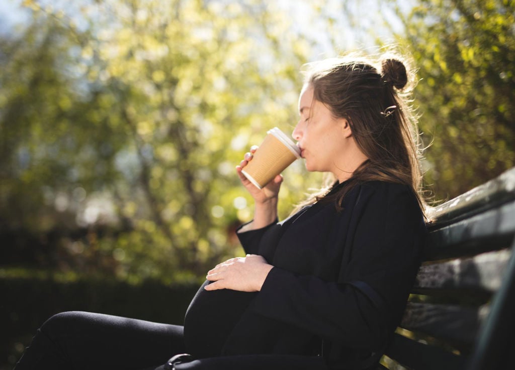 ung kvinna gravid på en parkbänk i solen