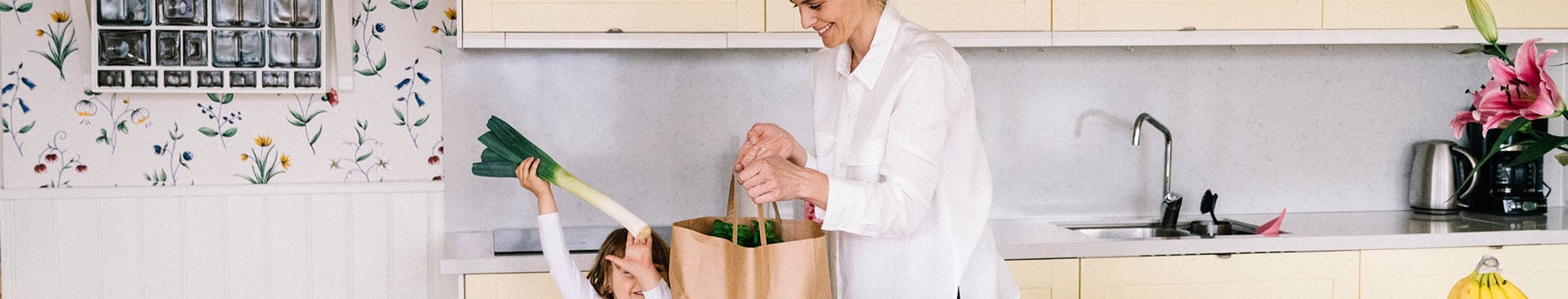 mamma med barn med matkasse i köket