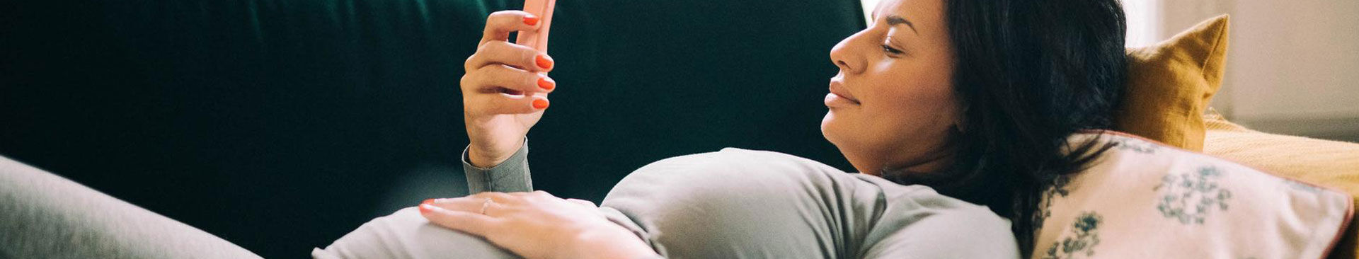 gravid kvinna ligger på soffa tittar på mobil