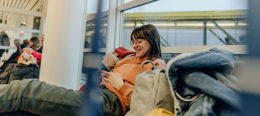 En glad person sitter med sin telefon på en flygplats